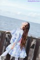 A young woman leaning against a wooden fence by the water.