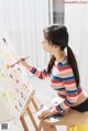 A woman sitting on a stool painting on an easel.