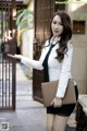 A woman in a white shirt and black skirt holding a brown bag.