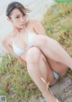 A woman in a white bikini sitting on the sand.