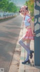 A woman in a pink and white outfit leaning against a wall.