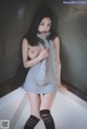 A woman in a gray sweater and black stockings posing in a bathtub.