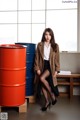 A woman in a leopard print coat sitting next to a red barrel.