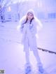 A woman in a white coat and hat standing in the snow.