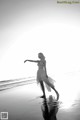 A woman in a white dress is walking on the beach.