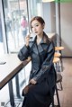 A woman in a black leather trench coat sitting at a table.