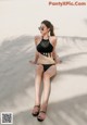 A woman in a black bikini sitting on a beach.