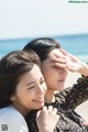 Two young women sitting on the beach looking at each other.