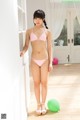 A woman in a pink bikini standing next to a green ball.